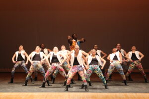 A large group of dancers perform hip hop on stage