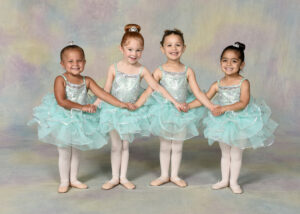 Four young ballerinas smile at the camera while holding hands